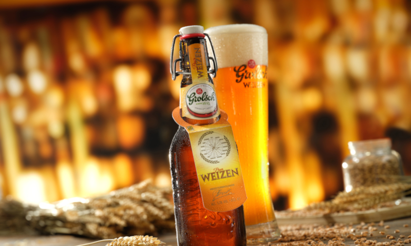 Grolsch Weizen beugelfles en volgeschonken glas met mout en tarwe er omheen